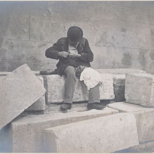 Clochard assis sur des pierres taillées.