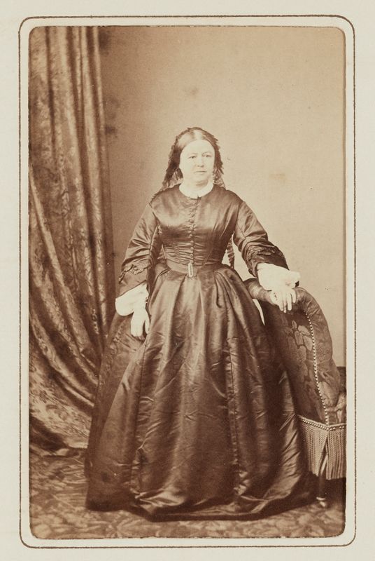 Fanny Renan, née Lair, debout avec bras gauche posé sur le dos d'un fauteuil