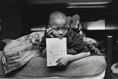 Margie's son, Jamont, 9, watches from his perch on a bunk bed as his mother chooses a dress for her job-training class. In the United States an alarming number of children are homeless. Olive Branch Mission, Chicago.